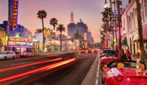 Noticias Celebrities muestra una animada calle de Hollywood al atardecer, con coches de lujo y luces de neón, representando noticias celebrities y el glamour de las celebridades. Esta imagen es adecuada para artículos sobre famosos, eventos y estilo de vida de las celebridades.