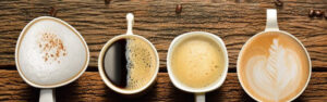 Tazas de café Estados Unidos muestra cuatro tazas de café diferentes dispuestas sobre una mesa de madera, representando la diversidad en el consumo de café en Estados Unidos.