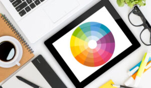 Noticias de Diseño Gráfico en una tablet con una rueda de color, rodeada de herramientas de diseño