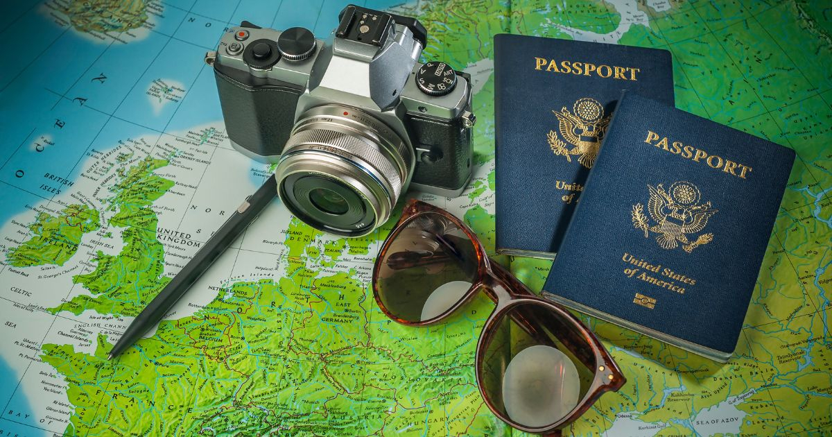 Mapa político de Europa con una cámara fotográfica, dos pasaportes estadounidenses, un bolígrafo y unas gafas de sol sobre él, representando la preparación para un viaje.